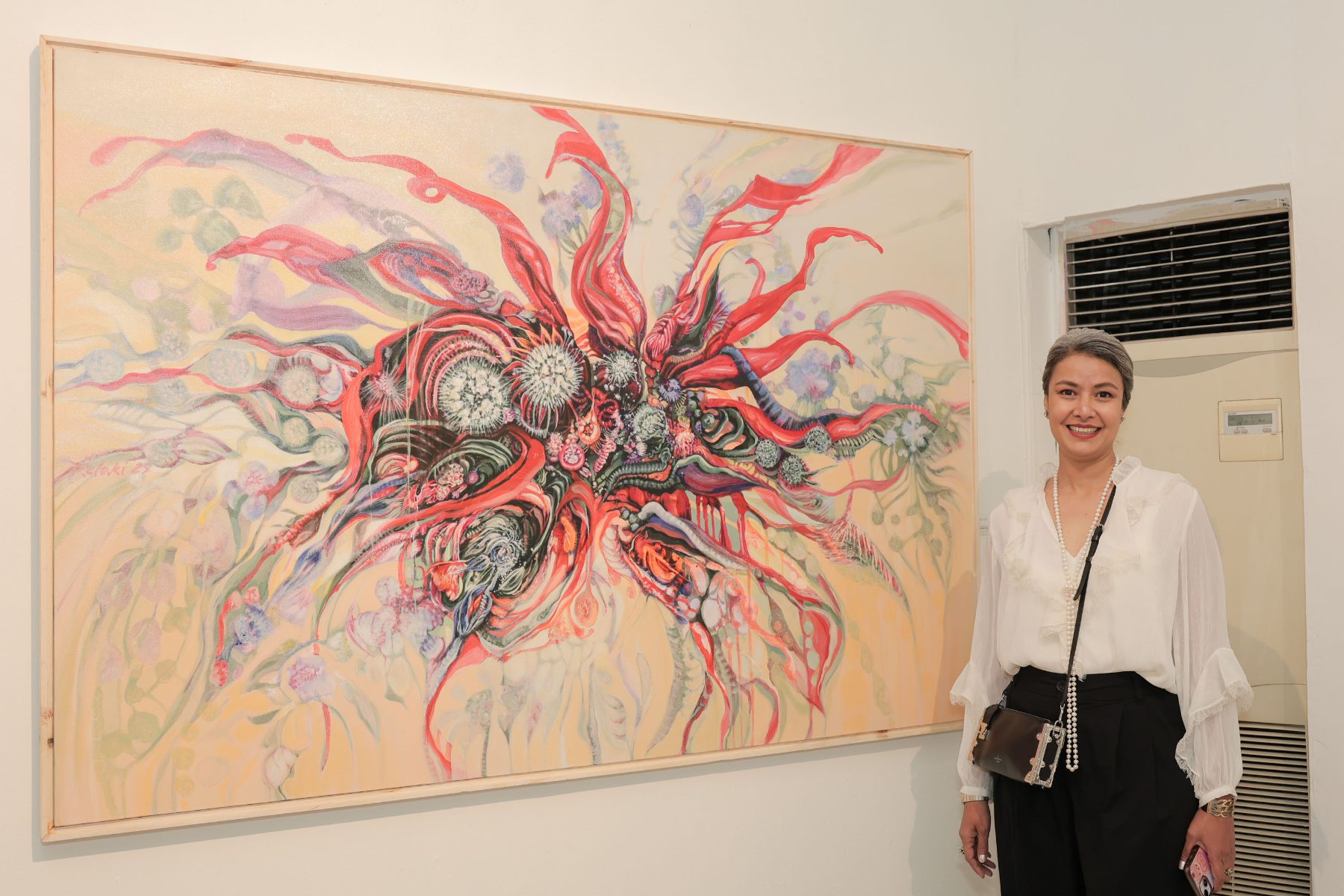An artist beside her canvas of red and blush forms