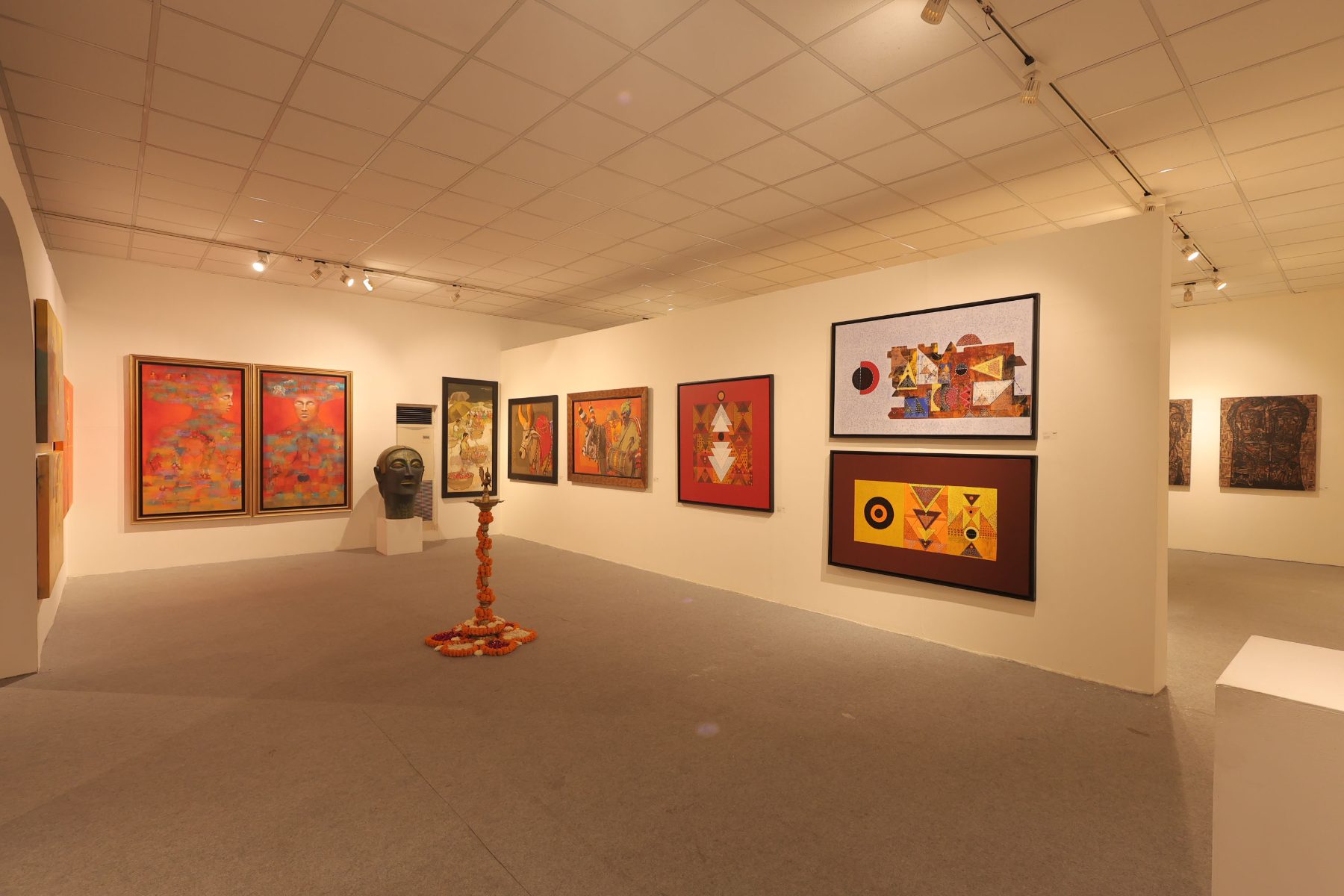A wide gallery with a brass lamp, a sculpted head and paintings in red and gold